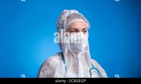 Porträt einer jungen Ärztin in Schutzanzug und Maske auf blauem Hintergrund. Arzt, der mit Covid-Patienten arbeitet. Medic in Schutzkleidung Stockfoto