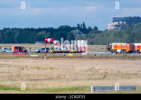 Hamburg, Deutschland. Juli 2020. Das abgestürzte Kleinflugzeug wird auf einen Anhänger geladen, während auf dem Flugplatz Feuerwehrfahrzeuge stehen. Am Freitag stürzte ein kleines Flugzeug vom Start- und Landebahn des Helmut Schmidt Airport ab, wodurch die Start- und Landebahnen vollständig geschlossen wurden. Quelle: Jonas Walzberg/dpa/Alamy Live News Stockfoto