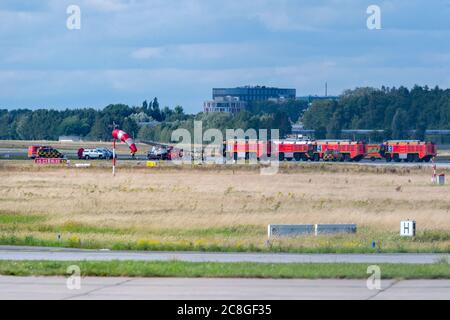 Hamburg, Deutschland. Juli 2020. Das abgestürzte Kleinflugzeug wird auf einem Anhänger wegtransportiert, während Feuerwehrfahrzeuge auf dem Flugplatz abgestellt werden. Am Freitag stürzte ein kleines Flugzeug vom Start- und Landebahn des Helmut Schmidt Airport ab, wodurch die Start- und Landebahnen vollständig geschlossen wurden. Quelle: Jonas Walzberg/dpa/Alamy Live News Stockfoto