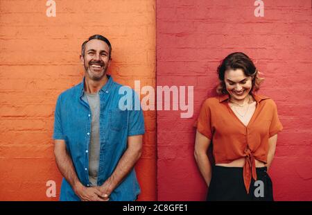 Mann und Frau stehen an der roten und orangen Wand. Ein Paar lehnte sich an eine farbige Wand und lächelte. Stockfoto