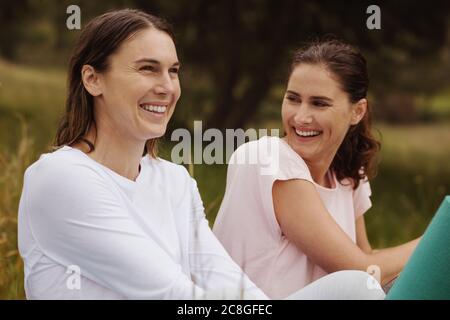Nahaufnahme von zwei lächelnden Frauen, die im Park sitzen. Fröhliche Freundinnen sitzen draußen und schauen weg. Stockfoto