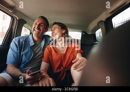 Liebende Paar auf dem Rücksitz eines Taxis. Lächelnder Mann und Frau, die in ein Taxi gehen. Stockfoto