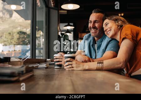 Glückliches Paar, das sich im Café mit einer Tasse Kaffee entspannt. Lächelnder Mann und Frau sitzen im Café und schauen zusammen aus dem Fenster. Stockfoto