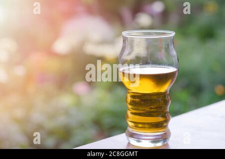 Ein unvollständiges Glas kaltes Bier auf dem Tisch im Garten, verschwommener Hintergrund Stockfoto