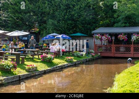 Menschen essen und trinken im Pub Garten des Compasses Inn neben dem Mühlbach in Gomshall Dorf, Surrey, England, Großbritannien, im Sommer Stockfoto
