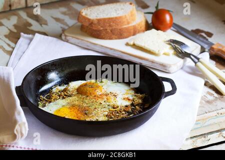 Spiegeleier mit Zwiebeln und Gewürzen in einer gusseisernen Pfanne. Stockfoto