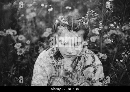 Junges Mädchen, das kontemplativ in einem Feld von Gänseblümchen sitzt Stockfoto