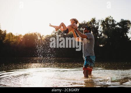 Vater hält ein kleines Kind in der Luft am See Spritzwasser Stockfoto