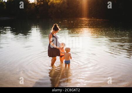 Schwangere Frau mit Kindern im Wasser am See mit goldenes Licht Stockfoto