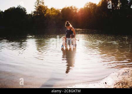 Kinder küssen schwanger Mutter Bauch im Wasser am See während Sonnenuntergang Stockfoto