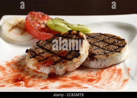 Zwei geröstete Rinderschnitzel vom Steak auf dem Teller mit gegrilltem Gemüse aus Tomaten, Zwiebeln und Paprika. Fotos für Restaurant- und Cafe-Menüs Stockfoto