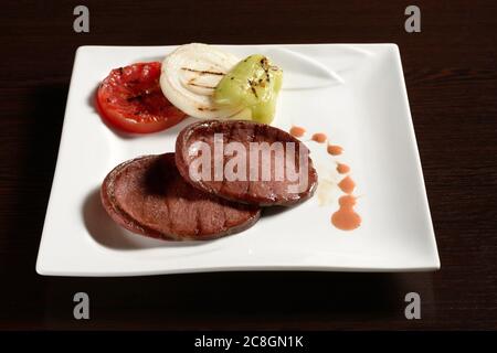 Gegrillte Rinderwurst-Scheiben mit gebratenem Gemüse von Tomaten, Zwiebeln und Paprika auf einem quadratischen Teller auf einem Holztisch. Fotos für Restaurant und c Stockfoto