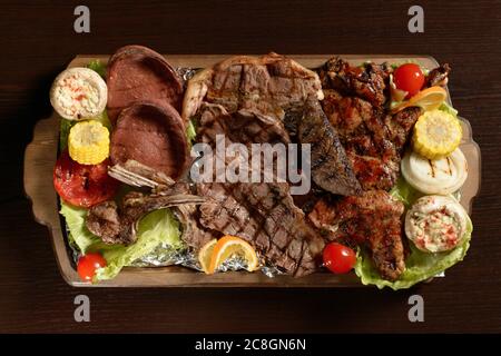 Auswahl an gegrilltem Fleisch mit Gemüse auf einem rustikalen Tablett und Holztisch Stockfoto