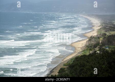 Eine Luftaufnahme von Wellen, die im Sommer auf den Sand eines Oregon Strandes krachen, während die Menschen im Sand spielen und sich wallen. Stockfoto