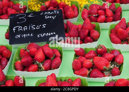 Erdbeeren aus Spanien zum Verkauf auf einem Markt in Frankreich mit gelben Blumen im Hintergrund Stockfoto