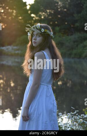 Mädchen in weißem Kleid trägt eine Blumenkrone am See Stockfoto