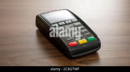 POS-Terminal isoliert auf Holzhintergrund, Kopierraum.Terminal-Kassenautomat für kontaktloses Bezahlen mit Kreditkarte. Bankausstattung, NFC Stockfoto