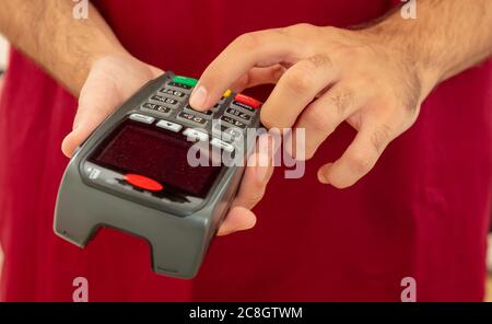 Mann hält eine Zahlung Swipe Maschine und Eingabe, Nahaufnahme. Kreditkartenleser, Kassenterminal-Bezahlkonzept. Stockfoto