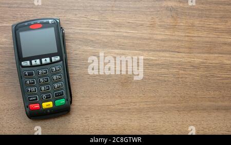 POS-Terminal isoliert auf Holzhintergrund, Draufsicht.Terminal-Kassenautomat für kontaktloses Bezahlen mit Kreditkarte. Bankausstattung, NFC. Stockfoto