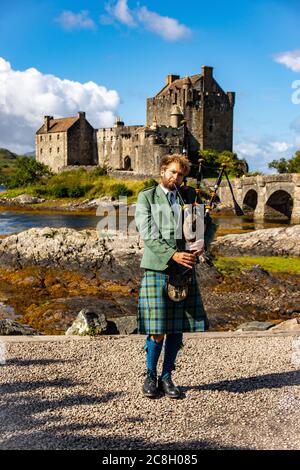 Dornie, SCHOTTLAND: Mann in typischen Kleidern, der eine 'Great Highlands Bagpipe' vor dem Eilean Donan Castle spielt. Stockfoto