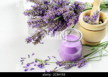 Blumenstrauß aus Lavendel, Holzmörtel mit Stößel und Lavendelkerze auf weißem Hintergrund Nahaufnahme. Kräuteraroma Konzept. Stockfoto