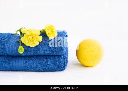 SPA-Konzept. Gelbe Badebombe und zwei blaue Handtücher mit Nelkenblume auf hellem Hintergrund. Platz für Text kopieren Stockfoto