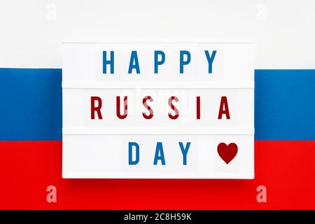 HAPPY RUSSIA DAY in Leuchtkasten auf russische Flagge Hintergrund geschrieben. Datum des Unabhängigkeitstages. Draufsicht. Stockfoto