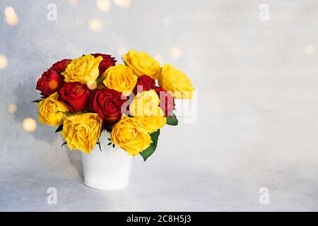 Bouquet von roten und gelben Rosen in weißer Vase. Getöntes Bild. Platz für Text kopieren. Hintergrund der Feiertage Stockfoto