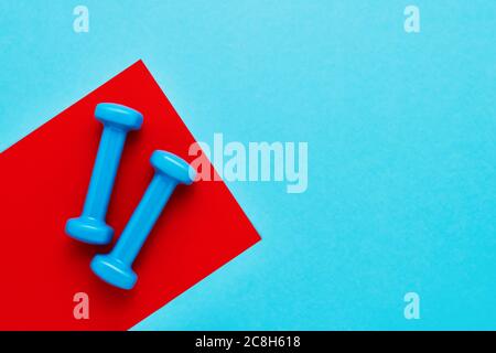 Blaue Kurzhanteln liegen auf rot-blauem Hintergrund. Das Konzept des gesunden Lebensstils. Platz für Text kopieren, Draufsicht Stockfoto