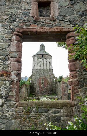 Blick durch ein Kirchenfenster auf einen keltischen Turm auf dem Friedhof von St. Andrew's Kirk in Portpatrick. Stockfoto