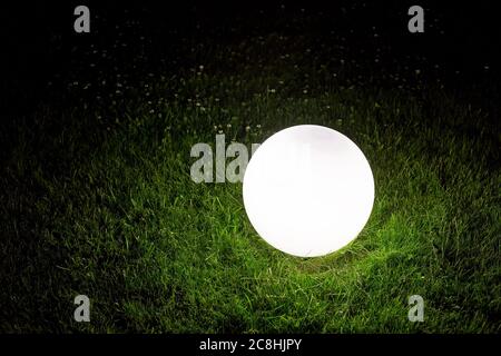 Illuminating conglobate Boden Gartenlampe der weißen Farbe liegt auf einem grünen Rasen im Gras im Hinterhof des Parks, Nahaufnahme der Beleuchtungseinrichtung Nacht sce Stockfoto