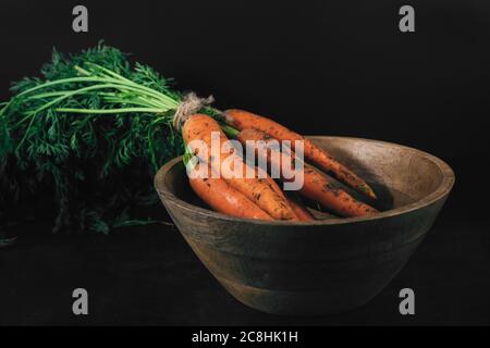 Nahaufnahme Bouquet von frischen Karotten mit grünen Blättern auf Holzschüssel auf dunklem Hintergrund. Bio-Öko-Lebensmittel. Karotten mit grünen Spitzen mit Seil gebunden. Gesundheit Stockfoto