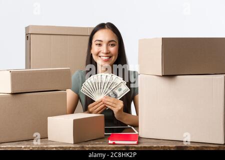 Kleinunternehmer, Startup und E-Commerce Konzept. Erfolgreiche lächelnde asiatische Geschäftsfrau Geld auf Online-Verkauf, zeigt Bargeld, während sitzen Stockfoto