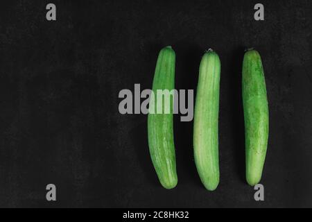 Drei Bio-Gurken auf dunklem Grund. Bio-Öko-Lebensmittel. Gesunde Ernährung. Frisch gepflücktes Gemüse. Frisches Gemüse für Salat. Natürliche Bio-Lebensmittel. Stockfoto