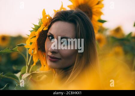 Mädchen in einem grünen Kleid und lange blonde Haare in einem Sonnenblumenfeld, lächelt und genießt den Moment. Das Konzept von Sommer und Sonne. Sonnenblumensaison in Israele Stockfoto