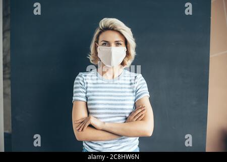 Vorderansicht Foto einer kaukasischen Frau mit medizinischer Maske auf dem Gesicht posiert mit gekreuzten Armen auf einer grauen Studiowand Stockfoto