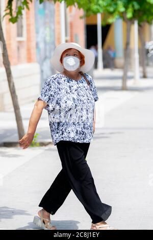 Reife asiatische Frau trägt eine Gesichtsmaske und einen Hut auf der Straße zu Fuß, während Blick nach oben auf einem unscharf Hintergrund. Sicherheit und Reisen Konz Stockfoto