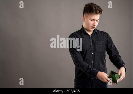 Portrait von ernst stilvolle attraktive Mann mit einem lässigen schwarzen Hemd gekleidet Blick auf die leere Brieftasche isoliert auf grauem Hintergrund mit Copy Space a Stockfoto