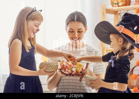 Glückliche Familie feiert Halloween! Junge Mutter behandelt Kinder mit Süßigkeiten. Lustige Kinder in Faschingskostümen. Stockfoto