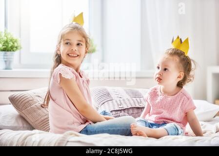 Zwei nette Kinder Baby Mädchen spielen und Spaß im Kinderzimmer. Liebevolle Schwestern mit Kronen auf dem Bett. Stockfoto