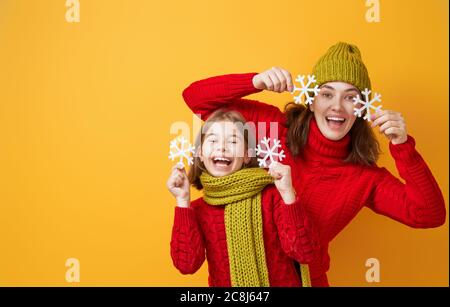 Winterporträt einer glücklichen, liebevollen Familie in Strickmützen, Snoods und Pullovern. Mutter und Kind Mädchen Spaß haben, spielen und lachen auf gelben Bac Stockfoto