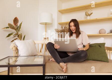 Aufgeregt Frau mit Laptop auf Sofa Stockfoto