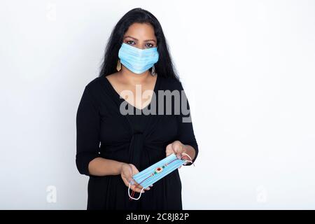 Indische Frau trägt Covid Schutzmaske, weibliche Displays Gesichtsmaske zusammen mit Rakhi Stockfoto
