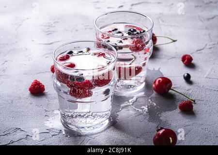 Frisches kaltes Sektgetränk mit Kirsche, Himbeere und Johannisbeere in zwei transparenten Glas auf Steinbeton-Hintergrund Stockfoto