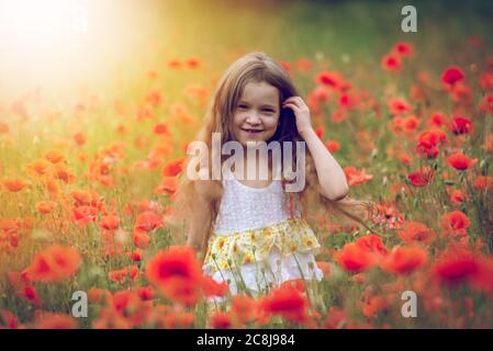 Liebenswert Mädchen 6 Jahre alt in einem hellen Mohn Feld. Portrait eines niedlichen Mädchens mit langen lockigen Haaren gegen das Sommerfeld voller roter Mohnblumen. Stockfoto