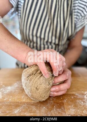 Frau knetet Teig für Roggenbrot auf einem Sauerteig. Bilden eines Laib Brot auf einem Holzbrett. Stockfoto