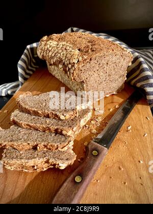 Brot aus deutschen traditionellen Multi-Cerealien-Brot Vollkornbrot, teilweise in Scheiben geschnitten auf einem Holzschneidebrett, Messer mit Holzgriff. Natürlich Stockfoto