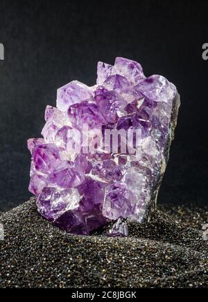 Amethyst Edelstein Nahaufnahme auf schwarzem Sand platziert. Mineral wird in einem vulkanischen natürlichen Gefühl wie Umgebung präsentiert Stockfoto