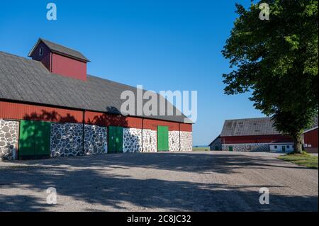 Eine große alte Steinmauer Scheune mit roten Details und grünen Türen auf einem traditionellen Bauernhof in Skåne, Schweden Stockfoto