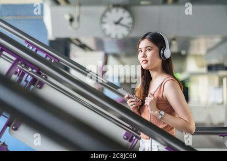 Junge asiatische Frau Passagier trägt Kopfhörer und mit Smartphone Musik hören und gehen die Treppe in der U-Bahn-Station, wenn traveli Stockfoto
